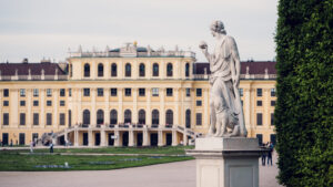 Scultura in pietra nei giardini del Palazzo di Schönbrunn davanti alla facciata gialla del palazzo.