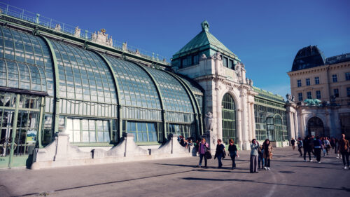 Glass and steel greenhouse building of Palmenhaus in the Burggarten with visitors outside.
