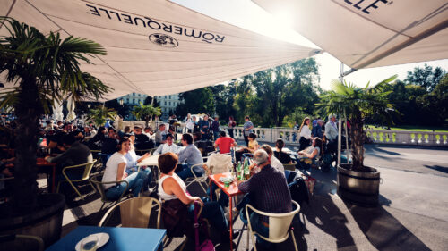 Busy outdoor terrace at Palmenhaus with guests seated under sun umbrellas.