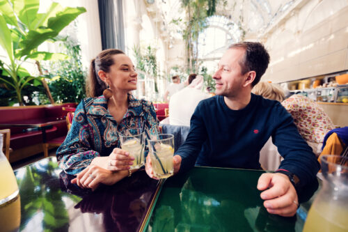 Adriana and Mario enjoying lemonade at a table inside Palmenhaus Vienna.