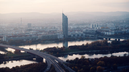 Millennium Tower and Danube bridges viewed from the Donauturm during golden hour, with autumn trees along the riverbanks.