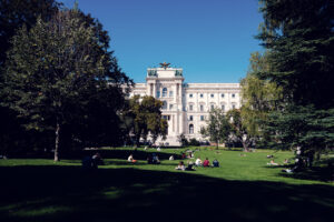 Visitantes descansando en el amplio césped del Burggarten con la Neue Burg al fondo.
