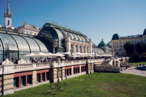 Terraza del restaurante Palmenhaus en el Burggarten con su techo de cristal curvado y mesas al aire libre.