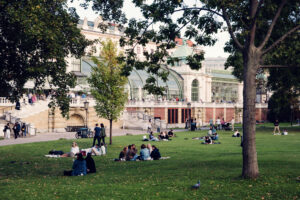 Visitantes sentados en el césped del Burggarten con el Palmenhaus al fondo.