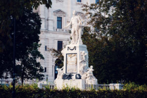 Monumento a Mozart nel Burggarten di Vienna, statua in marmo bianco circondata da siepi verdi.