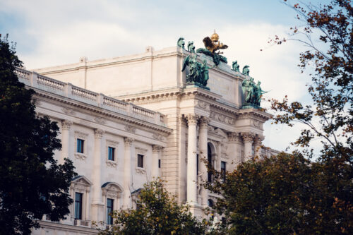 Vista del Palacio de la Hofburg desde el Burggarten, enmarcada por vegetación frondosa y con un vistazo a la historia regia de Viena.