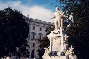 Primer plano de la estatua de Mozart en el Burggarten con letras doradas y figuras de ángeles en la base.