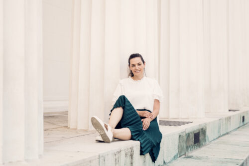 Adriana standing near Theseus Temple in Volksgarten, framed by white marble columns.
