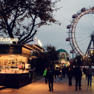 Le Bitzinger Würstelstand du Prater avec le Riesenrad illuminé en arrière-plan, créant une scène de soirée féérique.