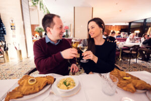 Momento romántico en el Meissl & Schadn: Adriana y Mario brindan con vino y cerveza mientras llega su schnitzel perfecto.