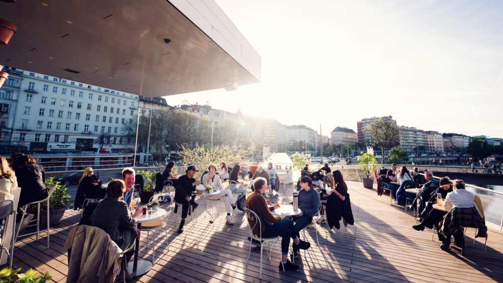 Elegant terrace at Motto am Fluss overlooking the Danube Canal, perfect for summer dining.