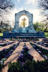Statue dorée de Johann Strauss jouant du violon dans le Stadtpark de Vienne, encadrée par des arbres.