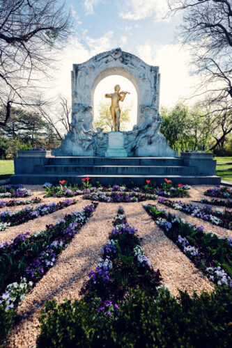 Golden statue of Johann Strauss playing violin in Vienna's Stadtpark, framed by green trees.