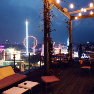 Terrasse sur le toit du ZOKU au crépuscule avec des guirlandes lumineuses au-dessus des toits de Vienne.
