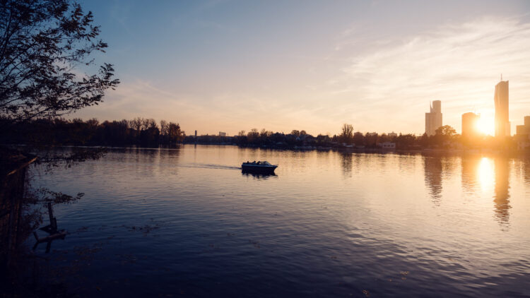 Boat on Alte Donau at dusk with Vienna skyline glowing in the background.