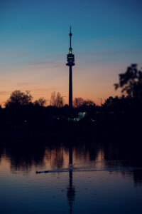 Vienna skyline at sunset from Alte Donau with Donauturm tower silhouetted against orange sky.
