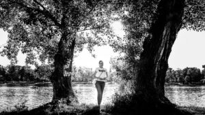Adriana posiert an einem Baum an der Alten Donau Wien mit ruhigem Flusswasser und natürlicher Ufervegetation im Hintergrund.