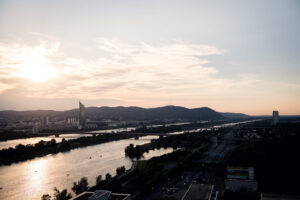 Evening sunset view from Vienna Danube Island showing orange sky reflection on New Danube waterway with city skyline silhouette.
