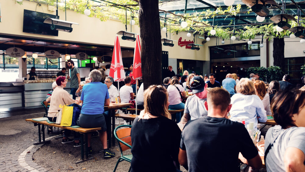 Lively summer afternoon at Schweizerhaus's outdoor seating, where locals and tourists enjoy traditional Austrian cuisine.