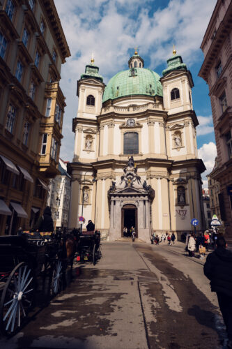 Außenansicht der Peterskirche in Wien mit ihrer markanten grünen Kupferkuppel und Barockfassade.