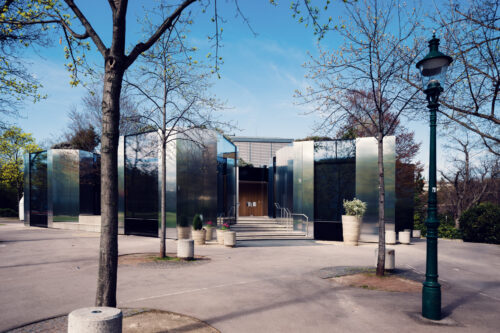 Glass and steel exterior of Steirereck restaurant in Stadtpark surrounded by trees.
