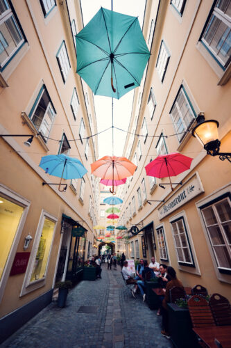 Rainbow umbrella canopy at Sünnhof Vienna with light patterns on the cobblestones.