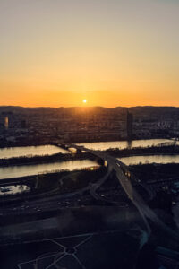 Evening panorama from Donauturm's rotating restaurant showing Vienna's modern skyline, with Millennium Tower silhouetted against orange sky.
