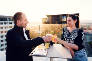 Adriana y Mario tomando cócteles en la Aurora Rooftop Bar de Viena con vistas panorámicas sobre la ciudad.