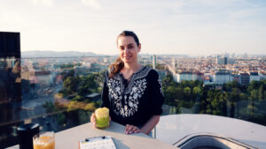 Adriana tomando un cóctel en la Aurora Rooftop Bar de Viena, con el horizonte de la ciudad de fondo.