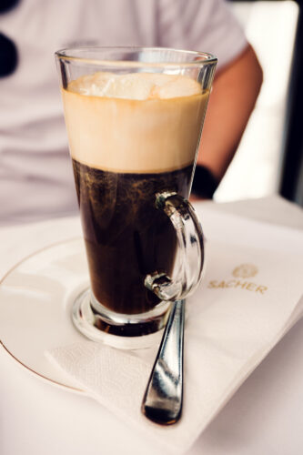 Classic Viennese Einspänner at Café Sacher with tall whipped cream in traditional glass mug with handle.
