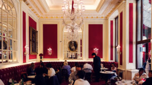 Elegant interior of Café Sacher Vienna with red velvet chairs, crystal chandeliers and classic marble tables.