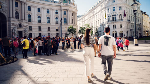 Adriana and Mario holding hands while passing the center of the Michaelerplatz with the imperial architecture surrounding them.