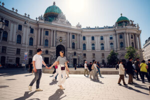 Adriana and Mario strolling through Michaelerplatz with the distinctive green dome of the Michaelertrakt behind them.