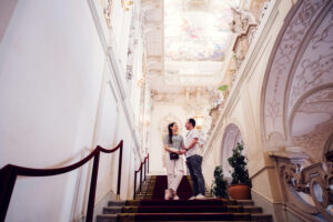 Adriana et Mario dans la salle de réception baroque du Palais Kinsky à Vienne, avec fresques au plafond et décorations classiques du palais.