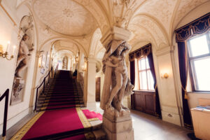 Escalier baroque du Palais Kinsky à Vienne avec marches de marbre, balustrades décoratives et peintures au plafond.