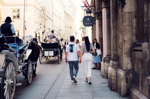 Adriana and Mario walking through Vienna's Old Town (Altstadt) with traditional horse-drawn carriages (Fiaker) in foreground.