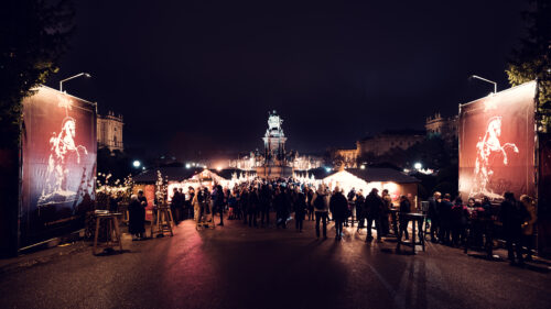 La nuit, des bannières rouges au cheval blanc cabré encadrent une allée animée vers le marché de Noël sur la Maria-Theresien-Platz.