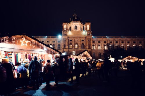 La nuit, des écharpes tricotées aux couleurs vives brillent sous des étoiles lumineuses pendant que la foule parcourt le marché de Noël sur la Maria-Theresien-Platz.