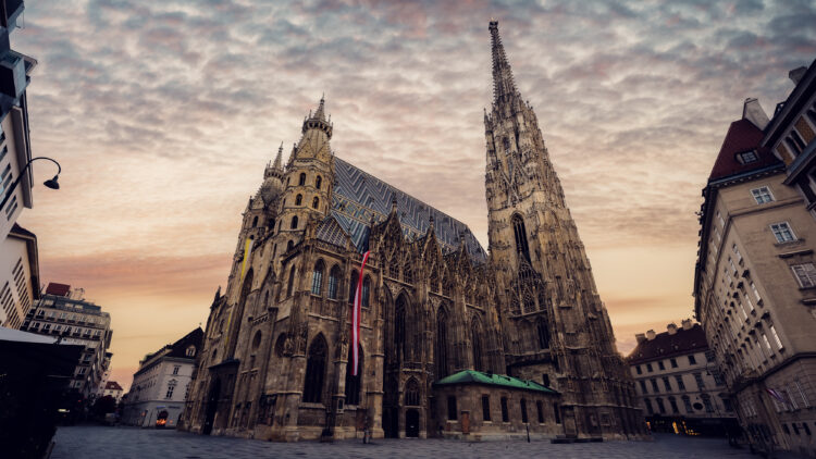 Gotische Fassade des Stephansdoms bei Sonnenuntergang mit österreichischer Fahne und dramatischem Himmel.