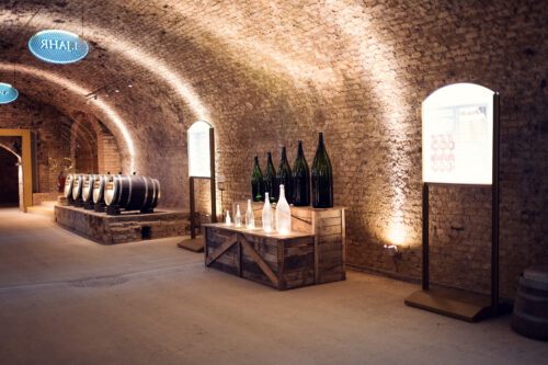 Exhibition room with oversized historic bottles and wooden barrels in a vaulted cellar at Schlumberger Kellerwelten.