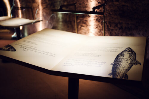 Illuminated historical document with handwritten text and an illustration of a wine bottle in the Schlumberger museum.