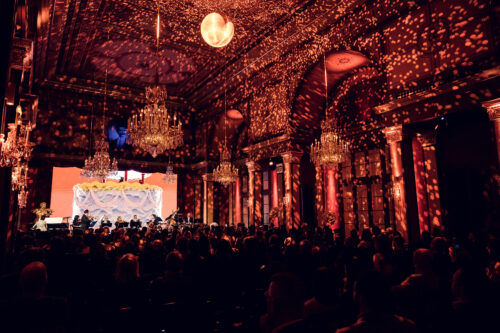 Wide view of the Strauss Hall during a concert with golden light projections.