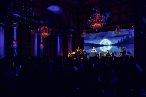 Soprano and orchestra performing under moonlit LED visuals in the Strauss Hall.