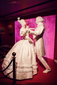 White sculpture of a waltzing couple in front of a pink-lit backdrop.