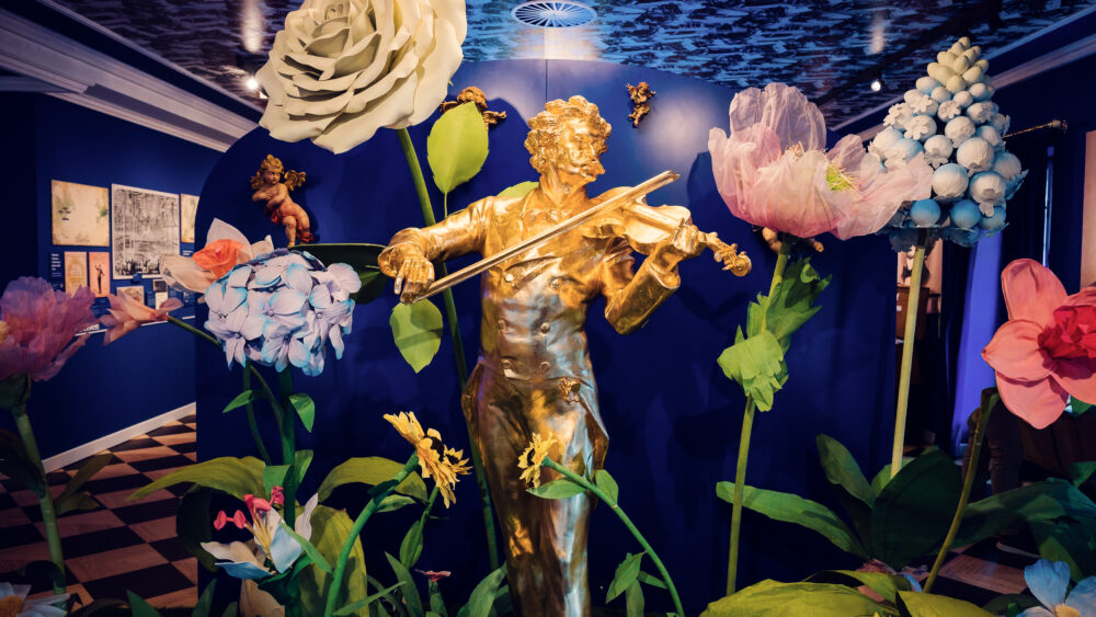 Golden Johann Strauss statue playing violin surrounded by oversized floral decorations.