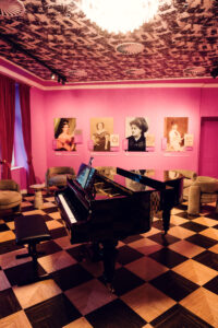 Pink-walled salon with grand piano and historical portraits at House of Strauss.