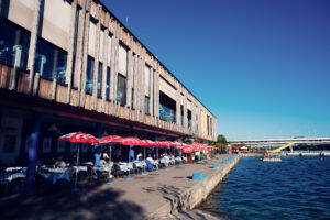 L'edificio del Pier 22 con ombrelloni rossi e una terrazza in riva all'acqua, accanto al Ponte Cagrana.