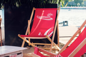 Una sdraio rossa di Copa Beach sulla sabbia, in riva all'acqua.