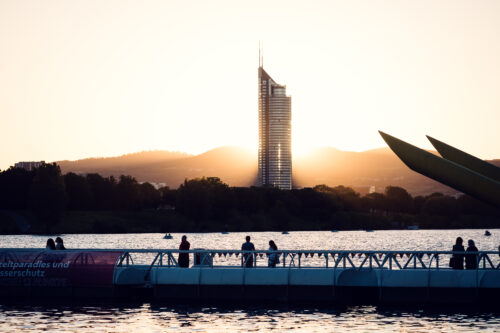 Visitatori sul ponte galleggiante al tramonto, con il Millennium Tower oltre Copa Beach.