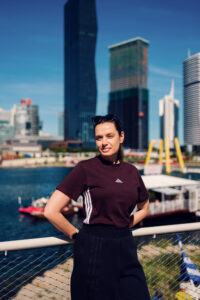 Adriana in piedi alla ringhiera di Copa Beach, con i grattacieli di Donau City alle sue spalle.